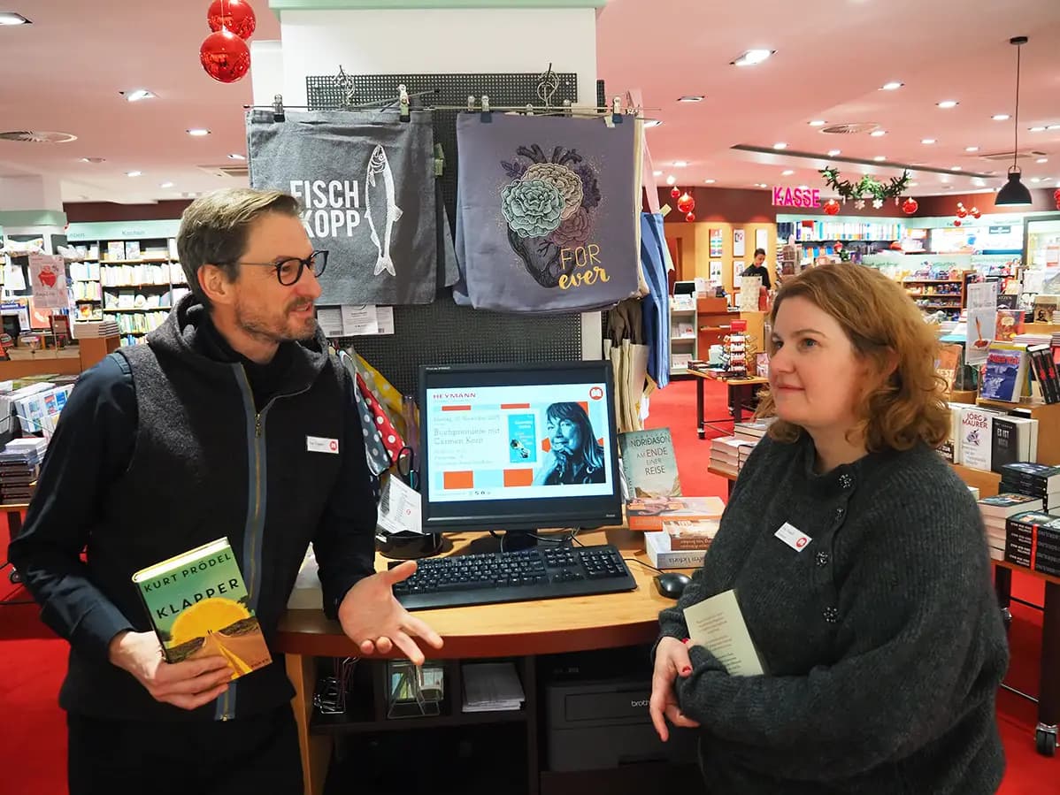 Eine Heymann-Mitarbeiterin steht gut gelaunt und mit einem Kinderbuch in der Hand vor dem Bücherregal.