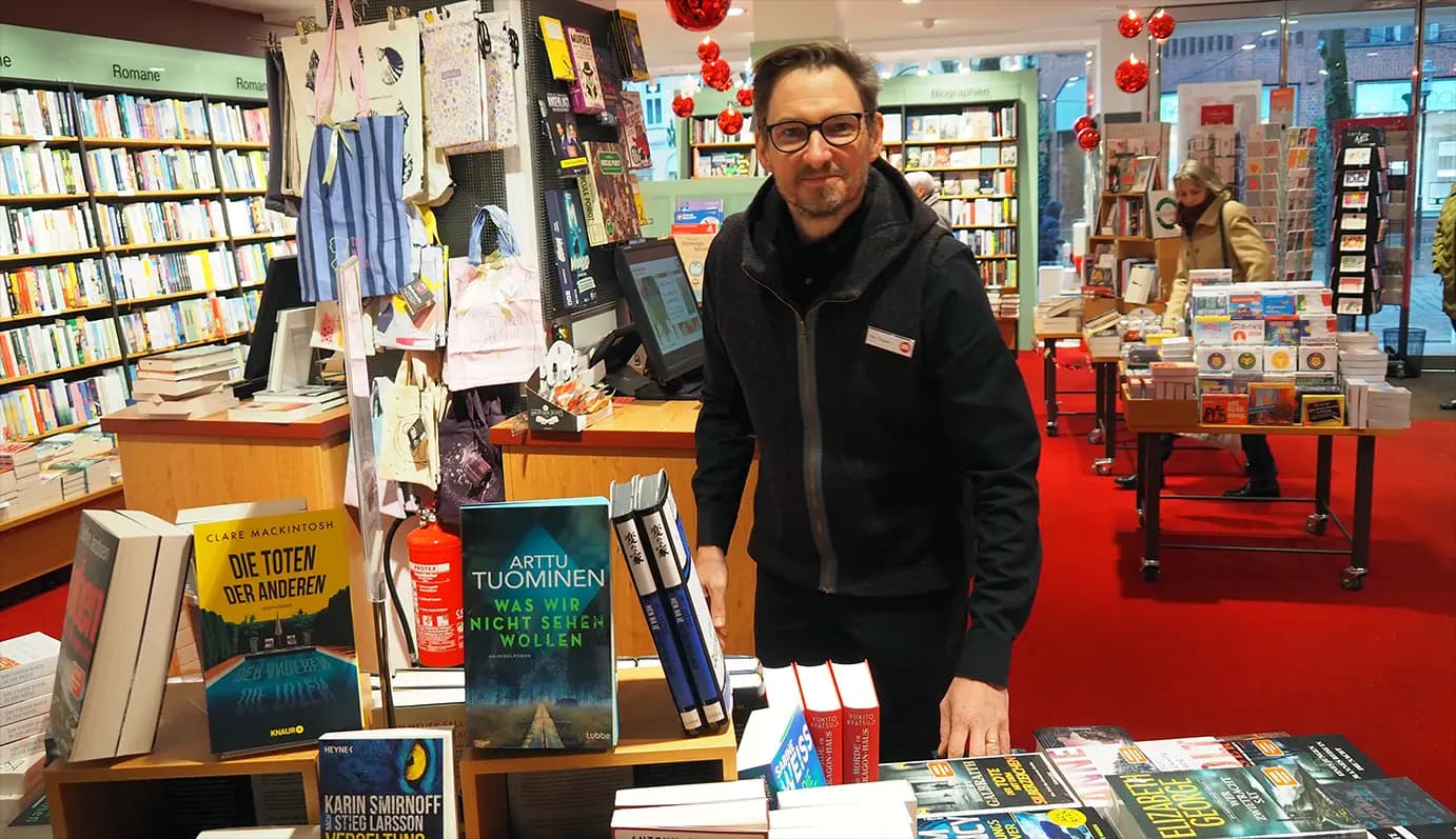 Ein hoher Stapel verschiedener Bücher liegt auf einem Holztisch und symbolisiert die Vielfalt der Literatur.