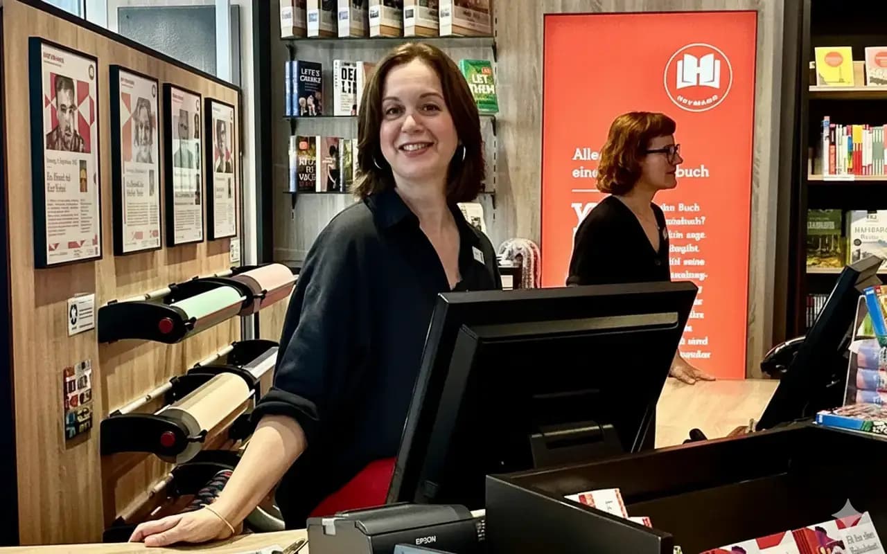 Eine Heymann-Mitarbeiterin berät lächelnd einen Kunden in einer hellen, freundlichen Buchhandlung.