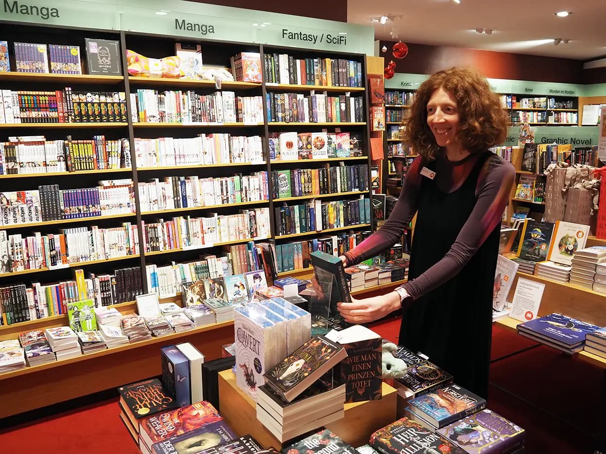 Eine Volontärin präsentiert lächelnd Puzzle in einem Regal.